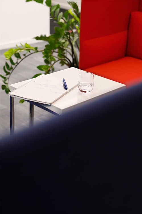 Detailný záber na stôl s poznámkovým blokom, perom a pohárom. V pozadí žiarivo červená pohovka