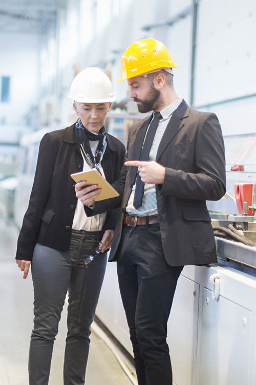 Man and woman with a helmet conversing in a factory building